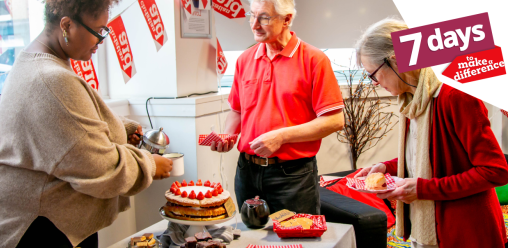 Two women and a man stood together. One woman is pouring tea for the man, whilst the other is putting cake on her plate. They are stood around a table full of baked goods.