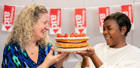 Two woman holding a cake and looking very joyful