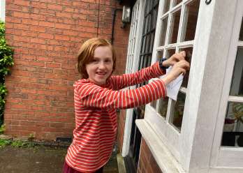 A young boy putting a paper sign up on a window, smiling at the camera